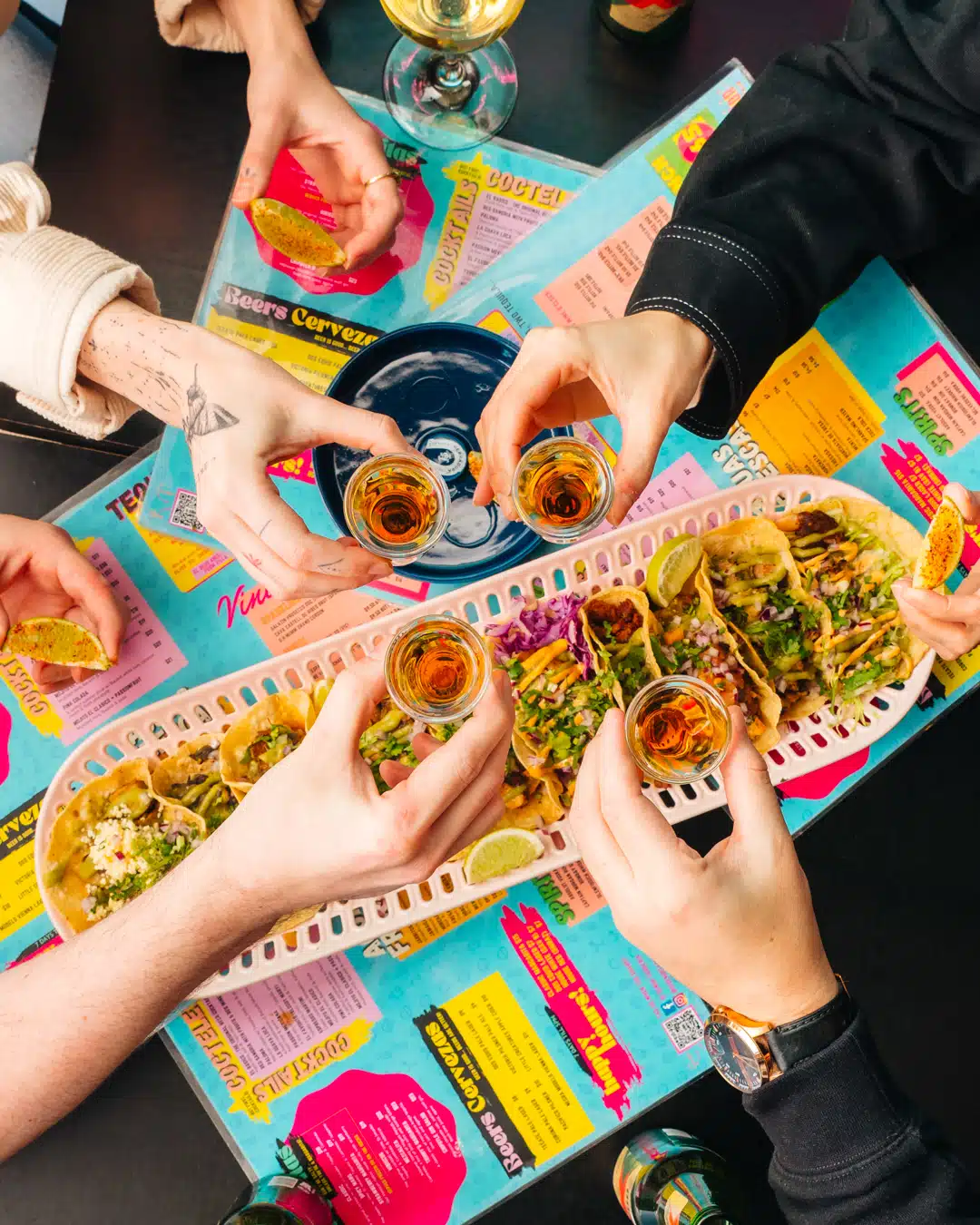 Food photography of group of friends holding shots of tequila with tacos from a restaurant marketing campaign.