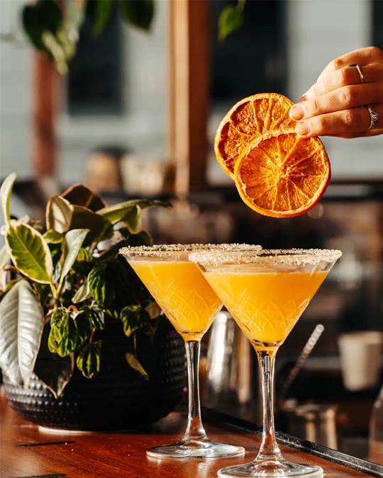 Drink photography of bartender garnishing two cocktails from a bar marketing campaign.