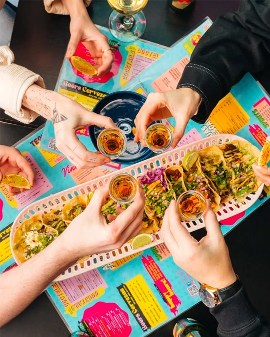 Food photography of group of friends holding shots of tequila with tacos from a restaurant marketing campaign.